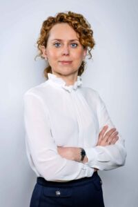 Na zdjęciu znajduje się dr hab. Julia Wojnowska-Radzińska na białym tle. Ubrana jest ona w białą bluzkę i czarną spódniczkę.